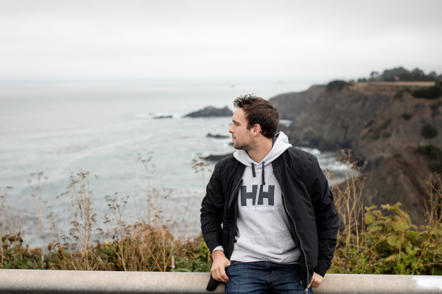 A man wearing a grey hoodie by the sea