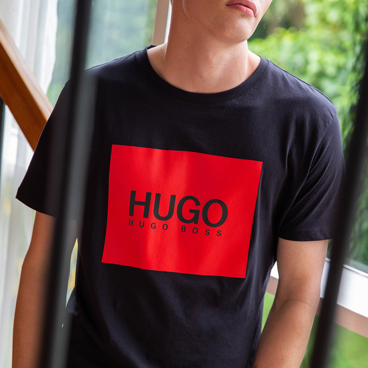 A zoomed in picture of a man wearing a black t-shirt with a red HUGO logo on the front. He face is not in shot. 