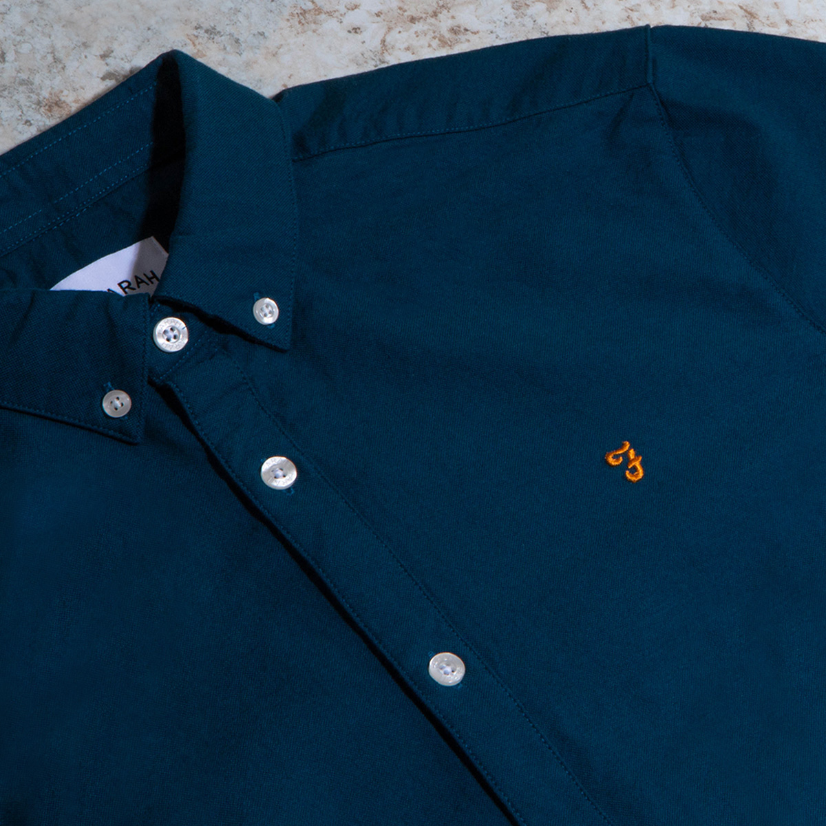 A blue Farah button-down shirt folded neatly on a marble floor.