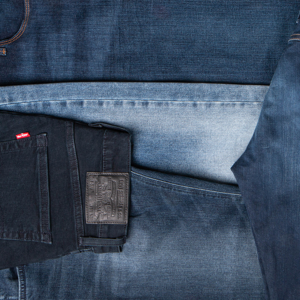 Five pairs of jeans folded up on the floor in different shades of blue.