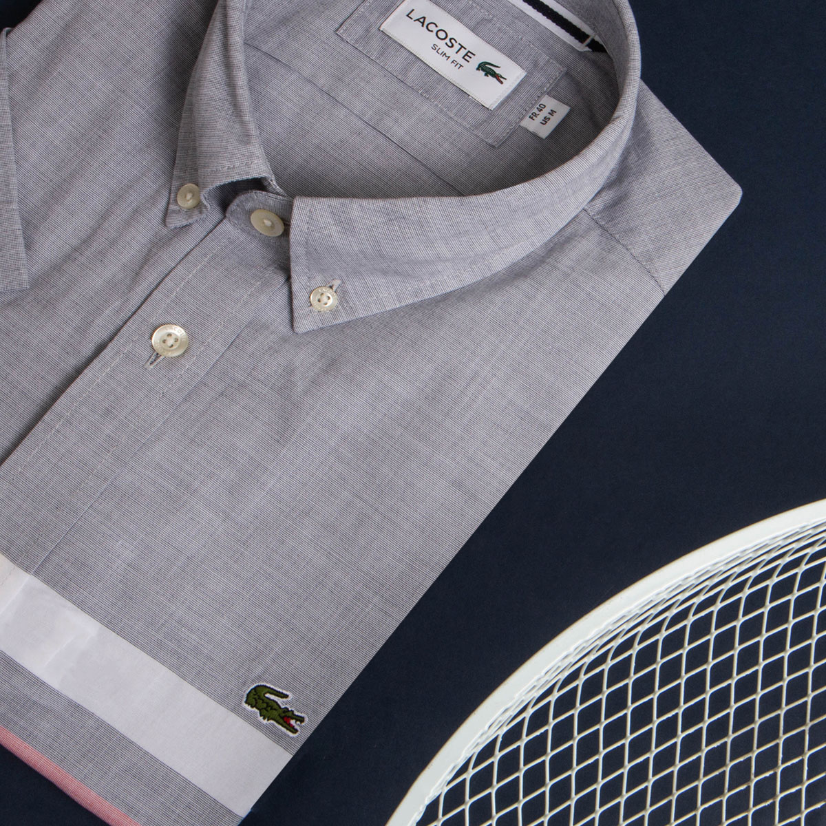 A grey Lacoste shirt folded on a table with the green crocodile logo on the right hand side.