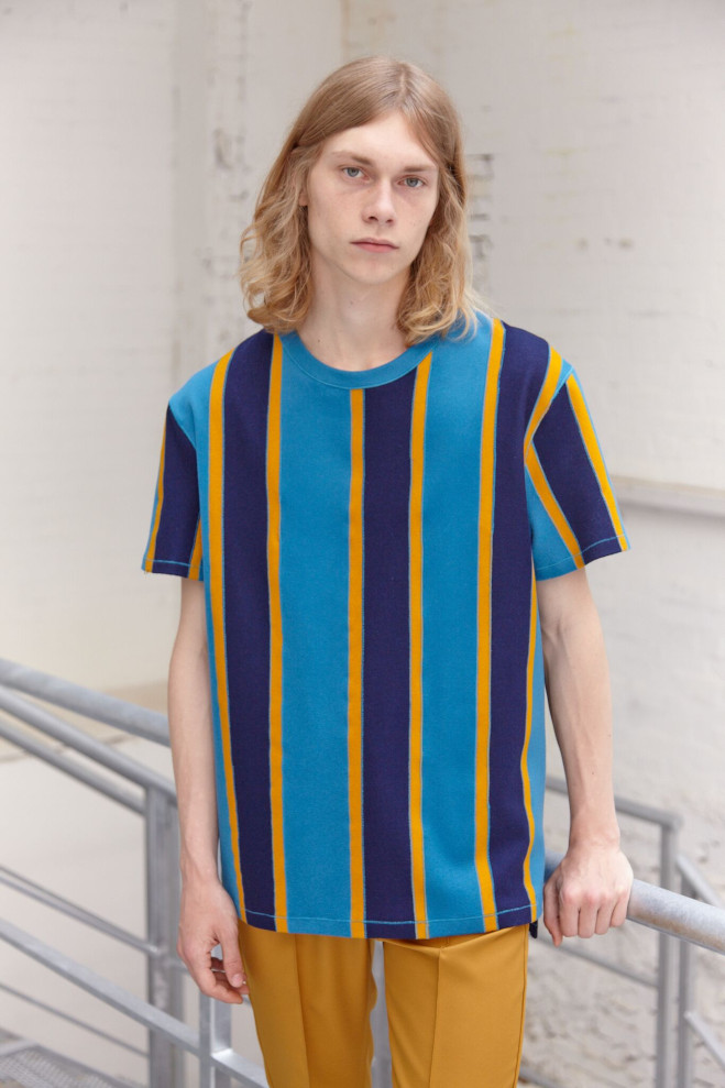 A man is stood wearing a blue and yellow stripe shirt. 