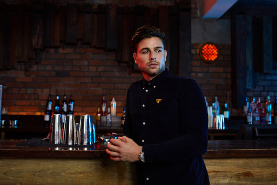 A man is leaning against a bar wearing a dark blue shirt.