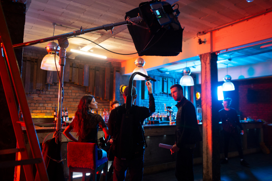 A shot of a bar dimly lit. Three people are talking near the bar near a camera.