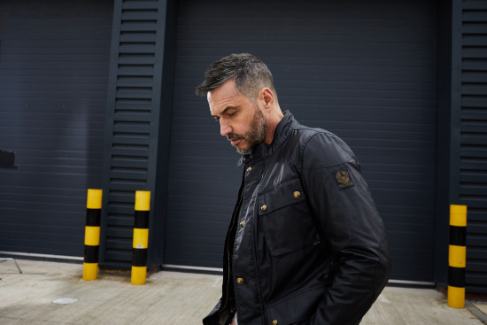 A man is stood looking down. He is wearing a black coat. 