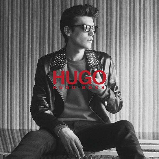 A man is sat on a bench wearing a leather jacket, t-shirt and black jeans from Hugo